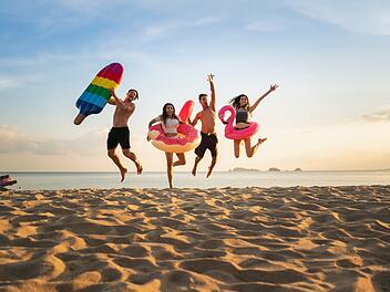 Urlaub ohne Kostenfalle: Diese Versicherungen brauchst du wirklich. Holiday summer party with friends on the beach .Group of family Sommerfest mit Freunden am Strand, Familiengruppe