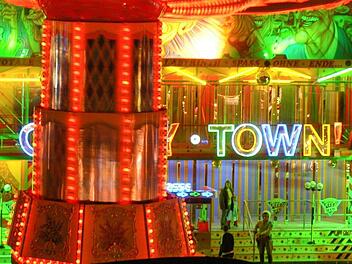 Schlechte Nachricht für Bamberg: Kult-Volksfest abgeblasen - trotz großer Ankündigung Ein hell erleuchteter Jahrmarkt mit bunten Lichtern und einer farbenfrohen Fassade. Ein Fahrgeschäft und der Schriftzug "Crazy Town" sind zu sehen. Ein Klassiker des Volksfestes.