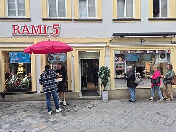 Bamberg: Lieferdienst Wolt mit Gratis-Döner-Aktion Vor einem Restaurant in Bamberg warten Menschen in einer Schlange. Ein roter Schirm steht da. Ein Schild bewirbt Gratis-Falafel in Kooperation mit Wolt.