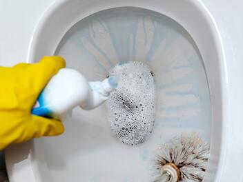 WC-Reiniger-Testsieger: Günstige Produkte überzeugen Stiftung Warentest Eine weibliche Hand in einem gelben Gummihandschuh reinigt die Toilettenschüssel mit einer Bürste und bedeutet - Female hand in a yellow rubber glove cleans the toilet bowl with a brush and means